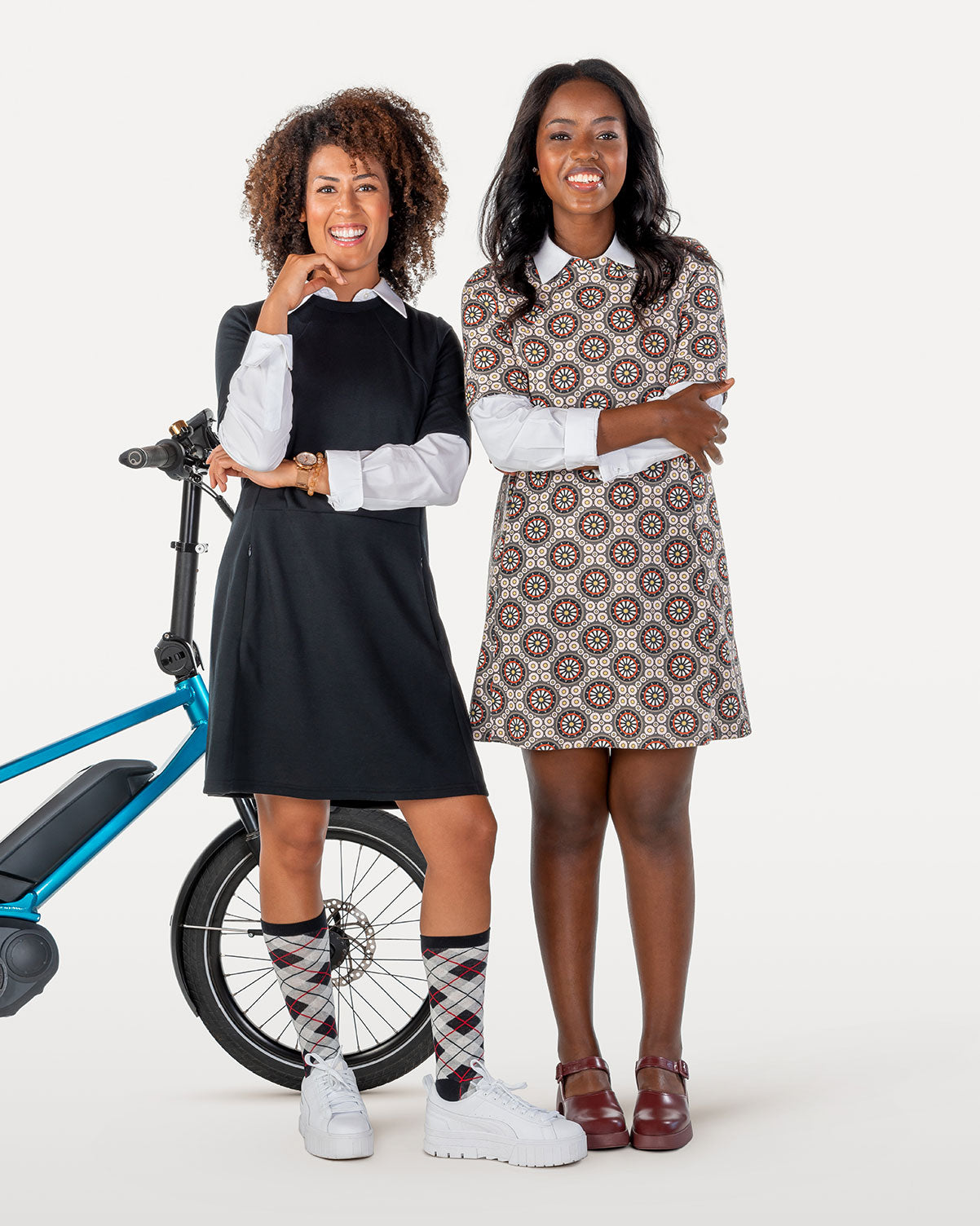 Two women modeling cycling dresses with blue bicycle in background.