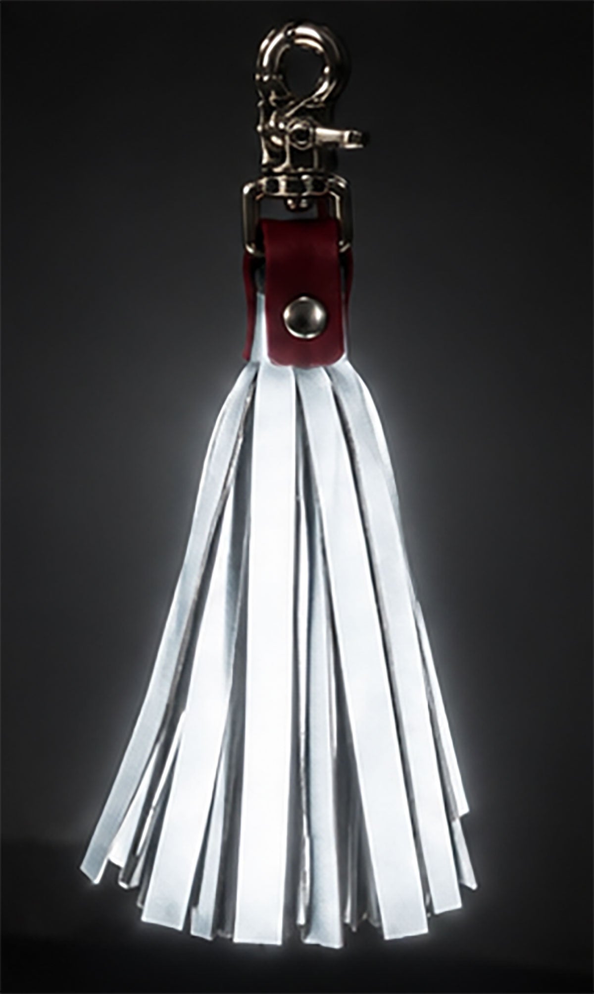 Reflective tassels with a silver metal clasp, a dark red leather loop, and a fan of white reflective strips, shown against a dark gray gradient background.