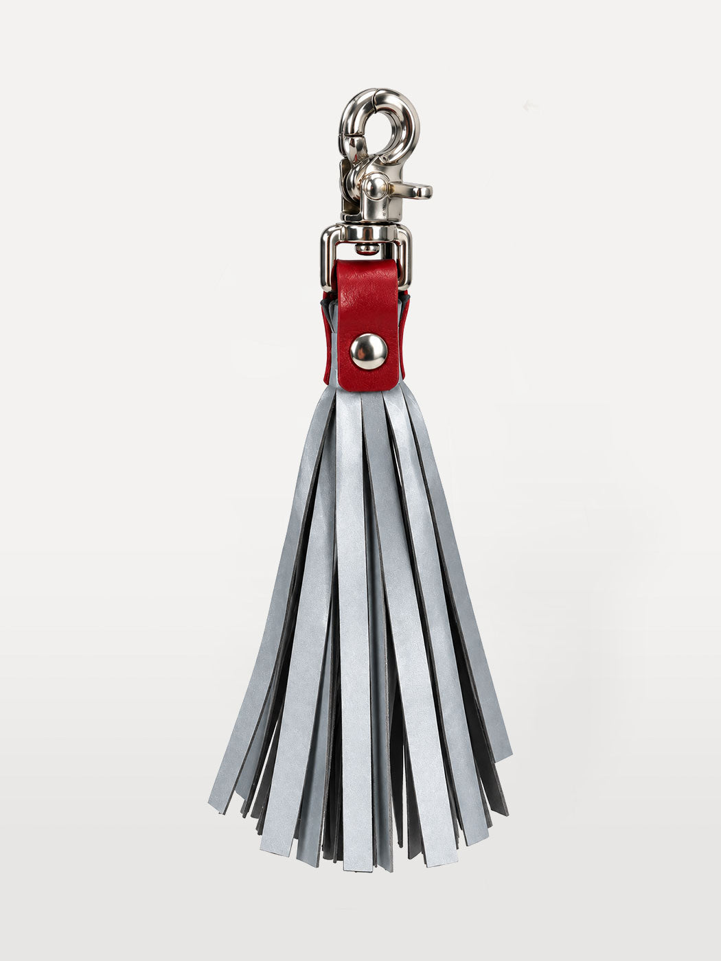 A silver metallic clasp holding a soft red leather band bunching togehter reflective tassels with silver hardware, shown against a plain light gray background.