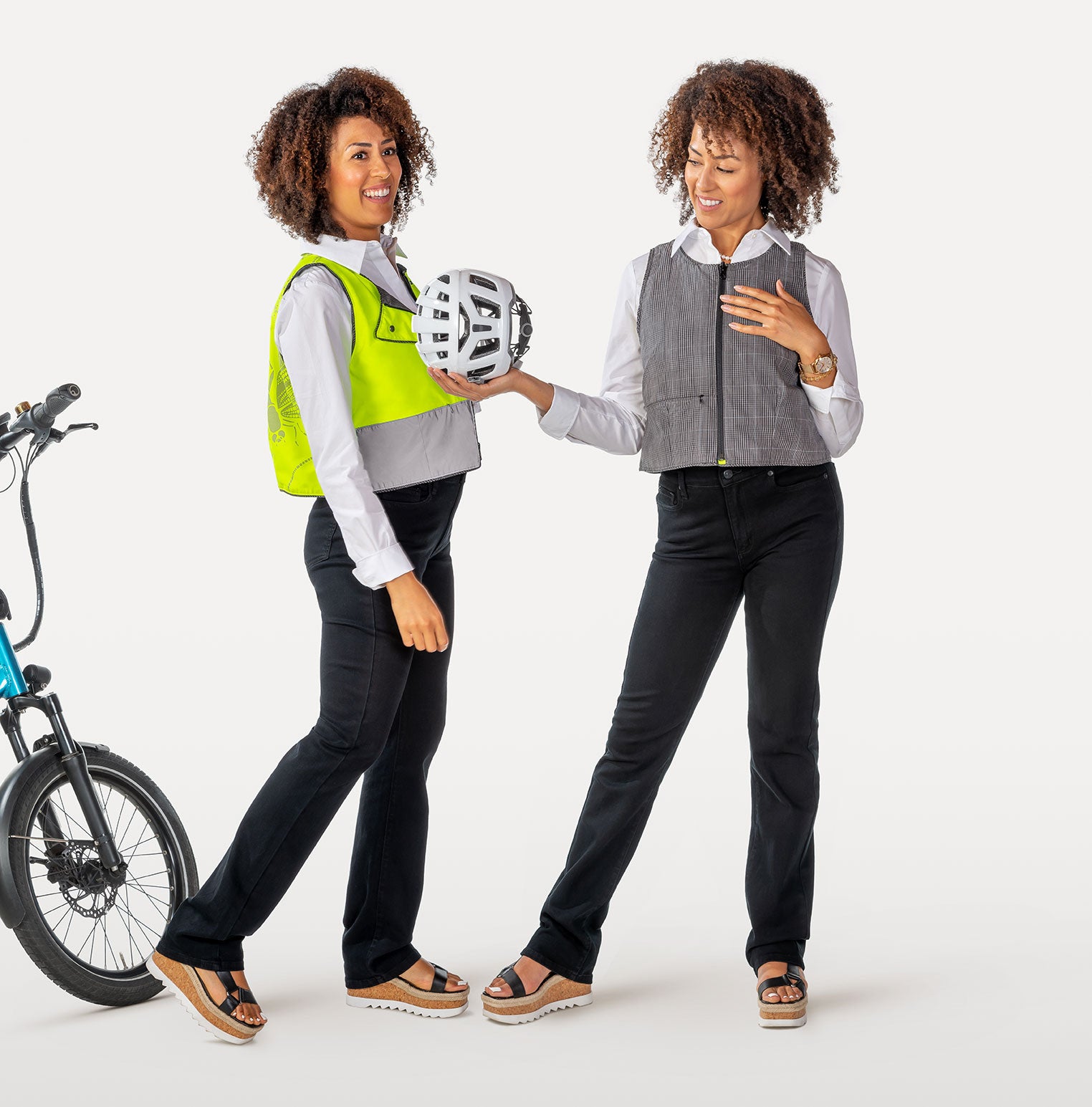 Two women in high-visibility reflective vests holding a helmet, with a bicycle on a white background