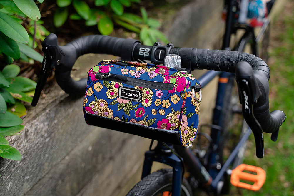 Floral-patterned handlebar bag attached to a bicycle handlebar with a natural background