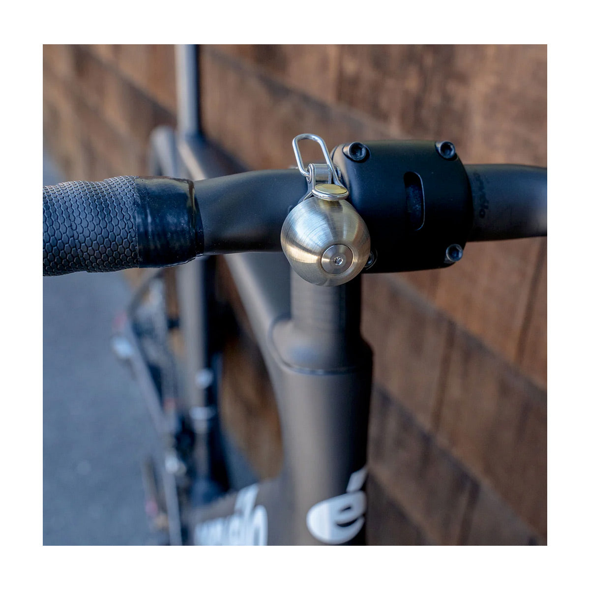 Close-up of a bicycle handlebar with a bell attached, against a blurred wooden background.
