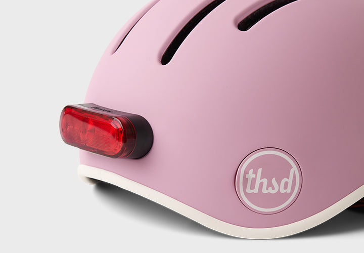 Pink helmet with a red tail light and 'thsd' logo on a white background