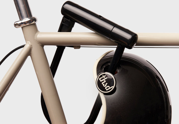 Close-up of a bicycle handlebar with a black lock through a helmet and 'thousand' brand logo on a white background