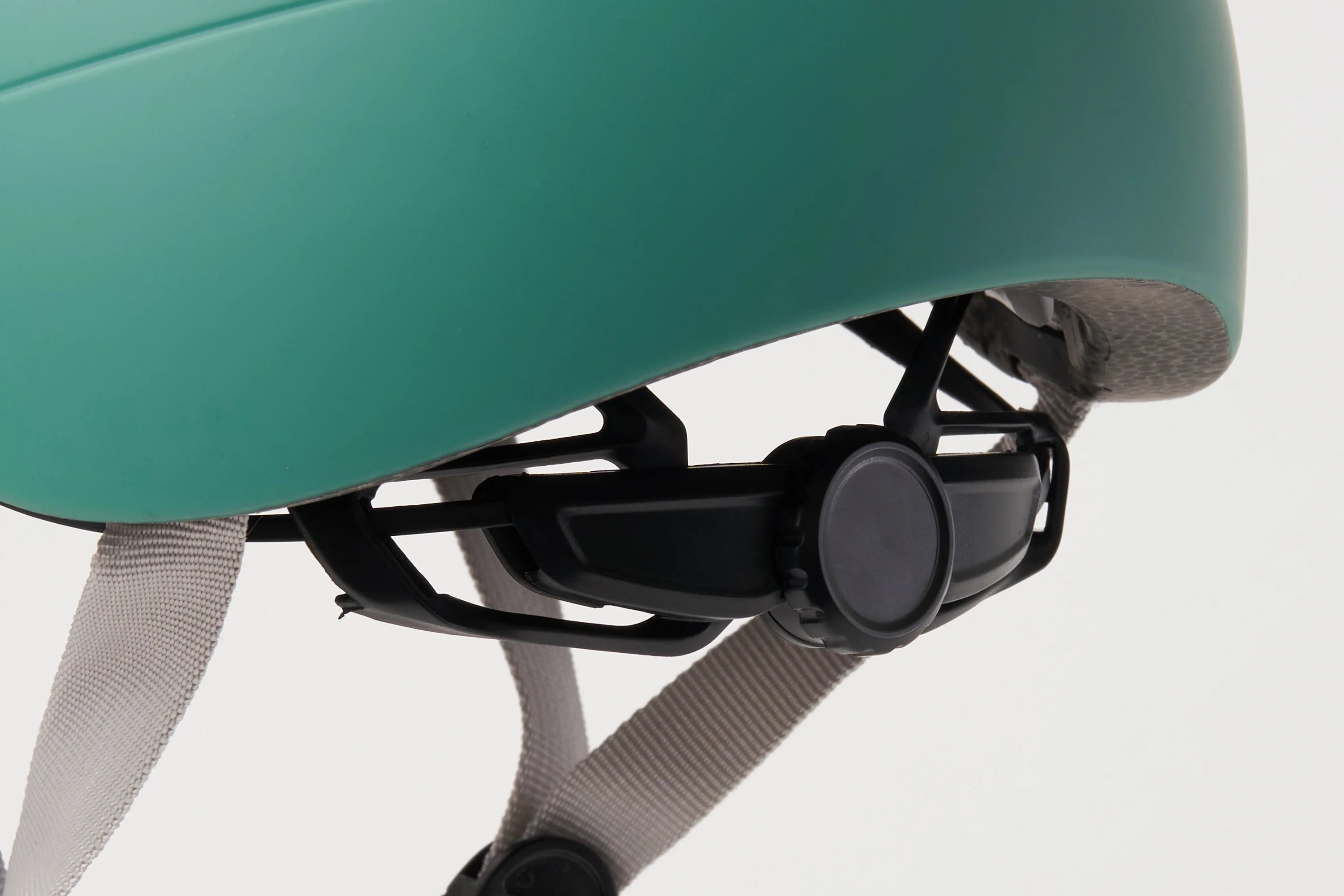 Close-up of a green helmet with a black strap and gray padding on a white background