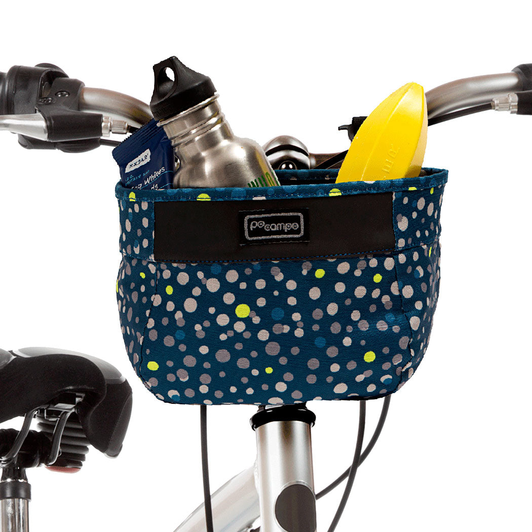Bicycle basket with polka dot pattern containing a water bottle, snack pack, and yellow banana holder on a white background.