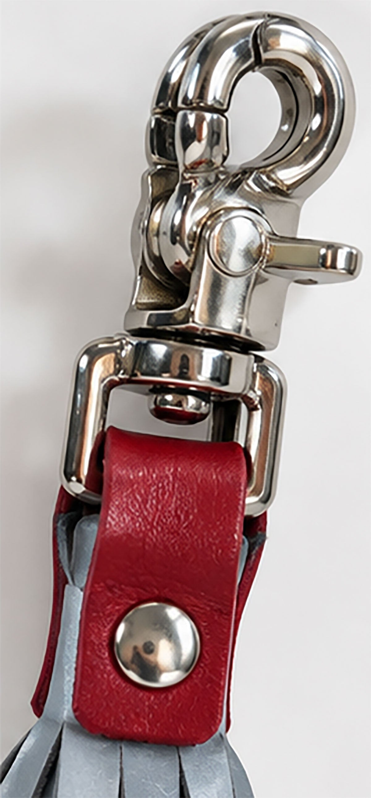 Close-up of a metal silver-tone lobster clasp, red leather loop, and reflective tassels on a plain light background.