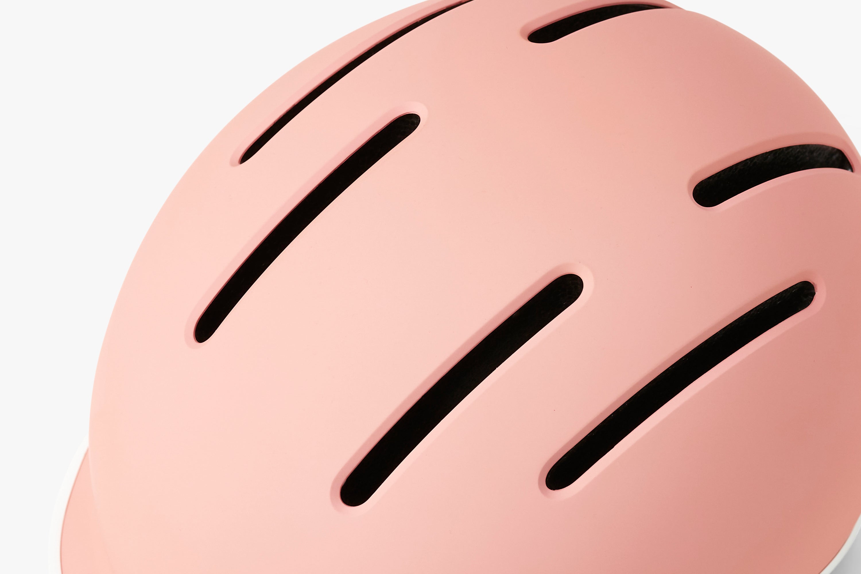 Close-up of a pink helmet with black ventilation slots on a light gray background