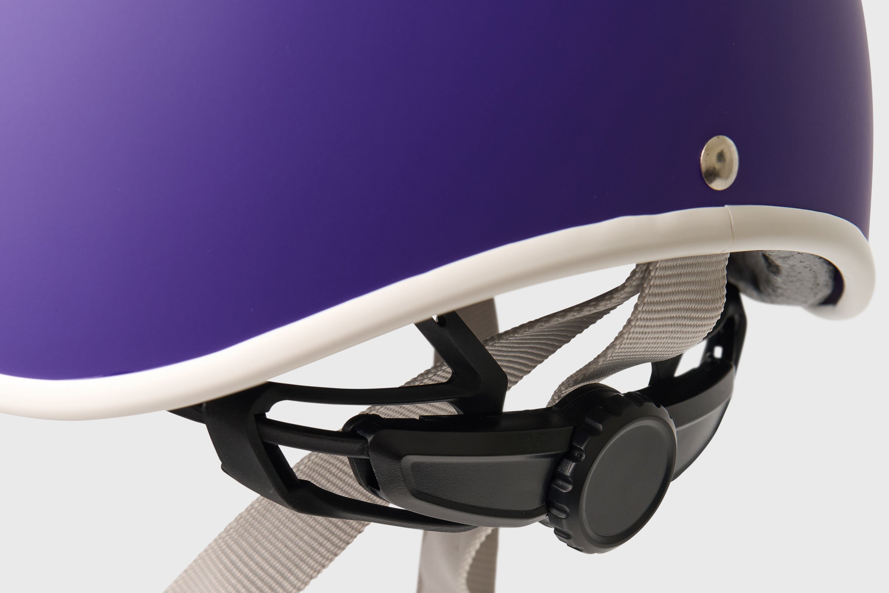 Close-up of a purple helmet with a white interior and black chin strap on a light gray background