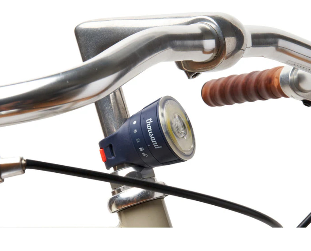 Bicycle handlebar with a blue light attached, featuring the brand 'thousand'.