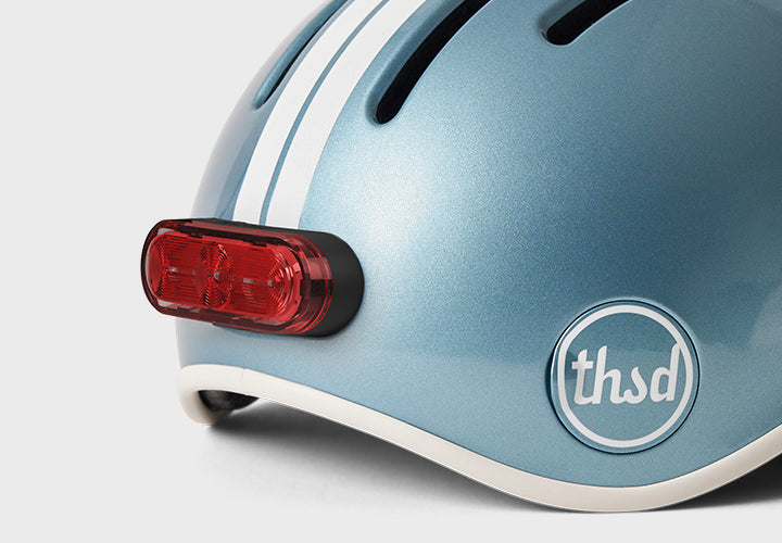 Close-up of a blue helmet with a red light and 'thsd' logo on a white background