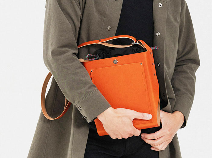 Person holding a modular orange leather bag with black insert.