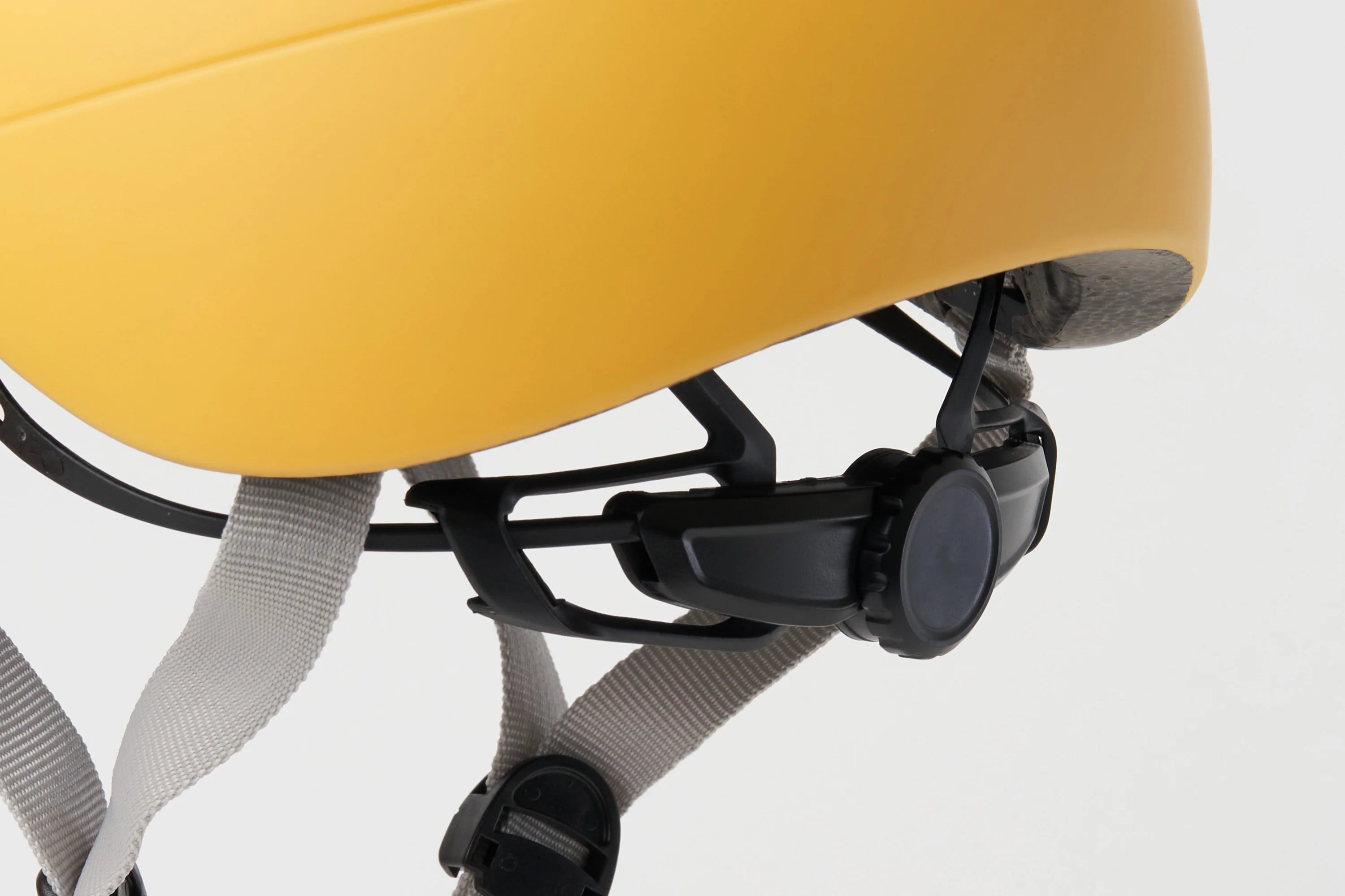 Close-up of a yellow helmet with straps and a black buckle on a light gray background